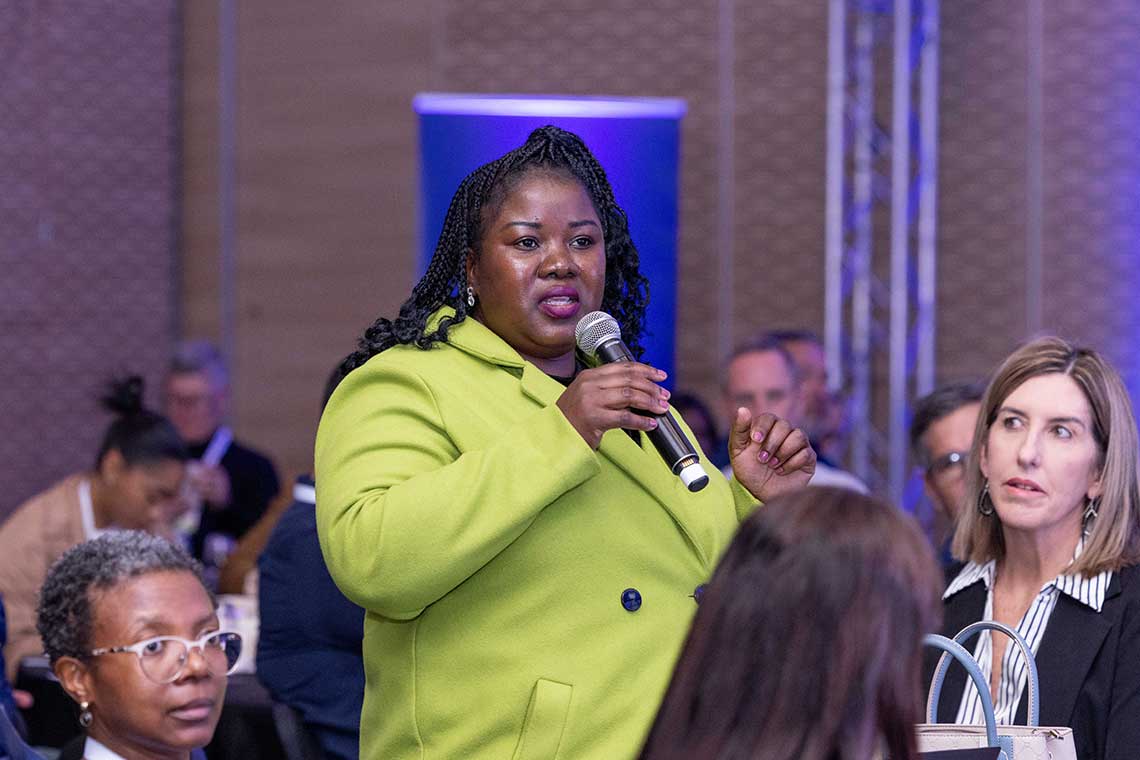 Woman speaking into a microphone at a conference.