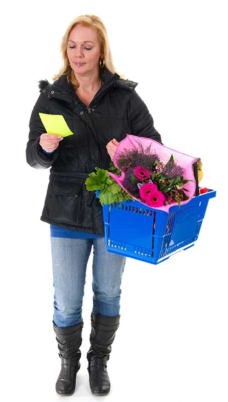 A woman holding a shopping basket with flowers and groceries.