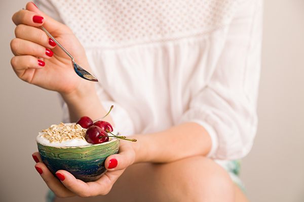 Closeup of woman's hands holding a cup with organic yogurt with oats and cherries.